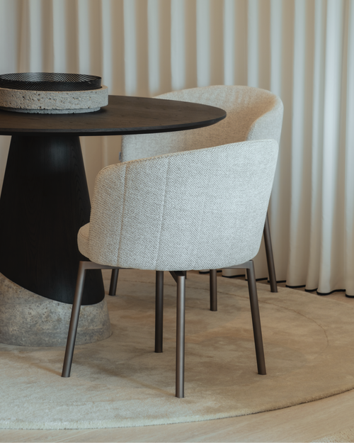 Round black dining table with beige chairs against a white curtain background