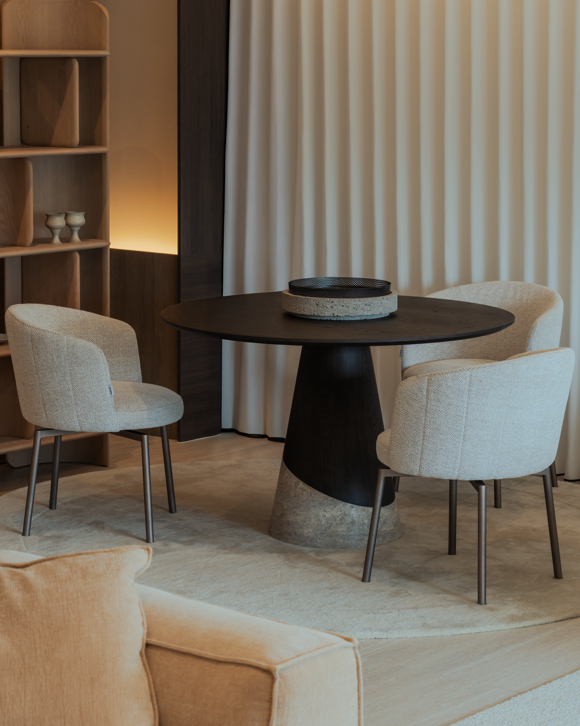 Modern dining area with a round black table and beige chairs in a softly lit room.
