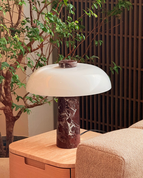 Table lamp with marble base on a wooden table next to a plant and sofa.