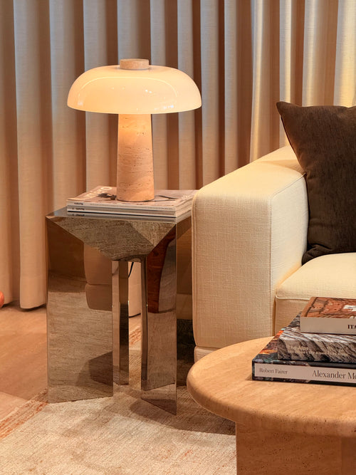 Modern interior with a lamp on a side table, books on a coffee table, and a beige sofa.