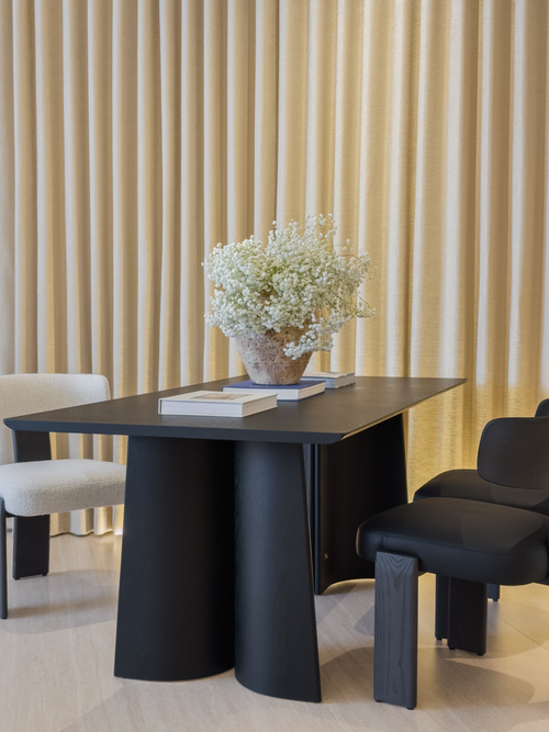 Modern black dining table with chairs and a vase of flowers in a room with beige curtains.