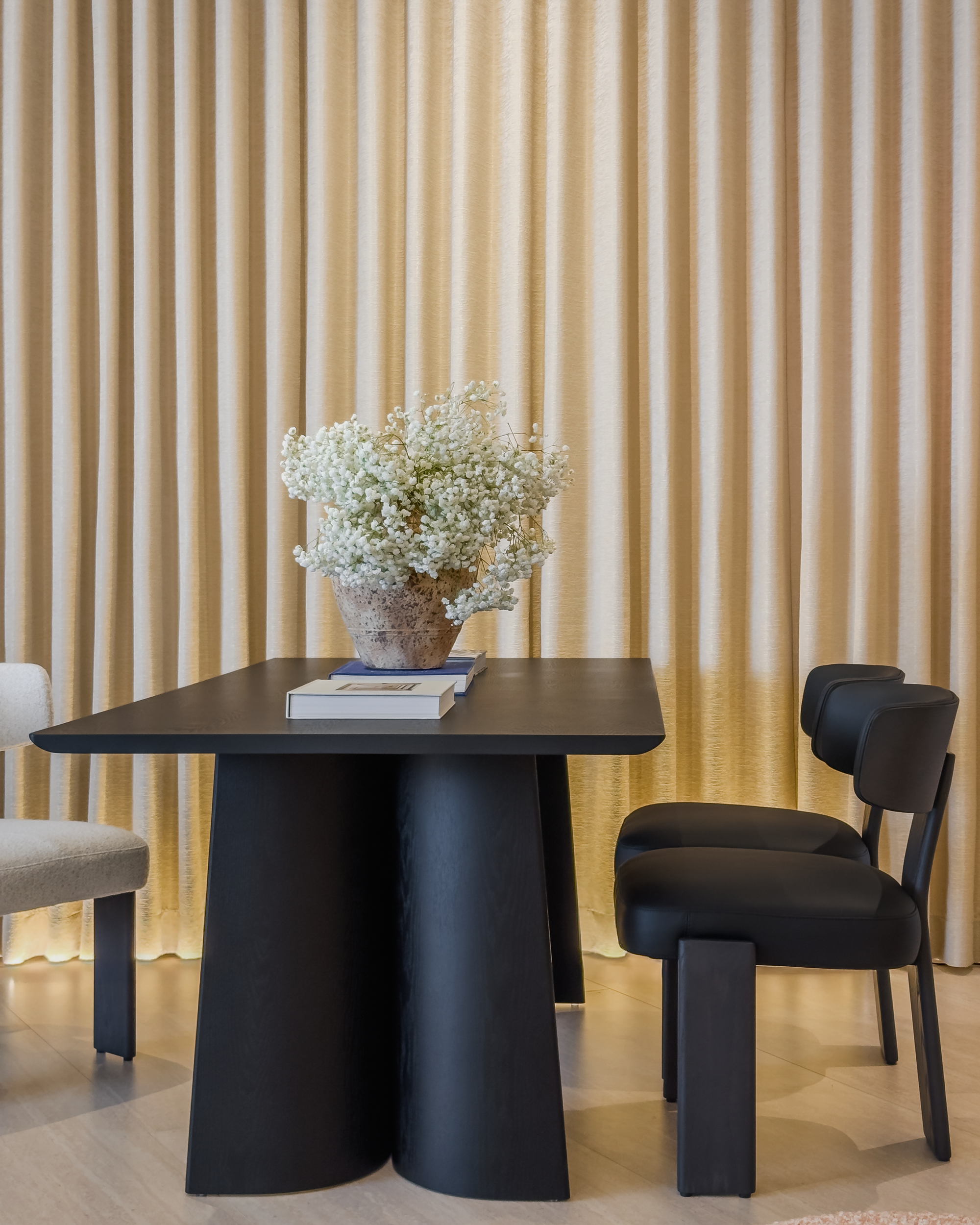 Modern black dining table with chairs against a beige curtain backdrop