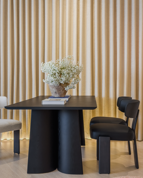 Modern black dining table with chairs against a beige curtain backdrop