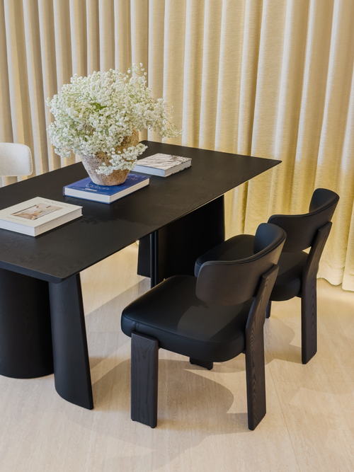 Black desk with two chairs in a room with beige curtains.