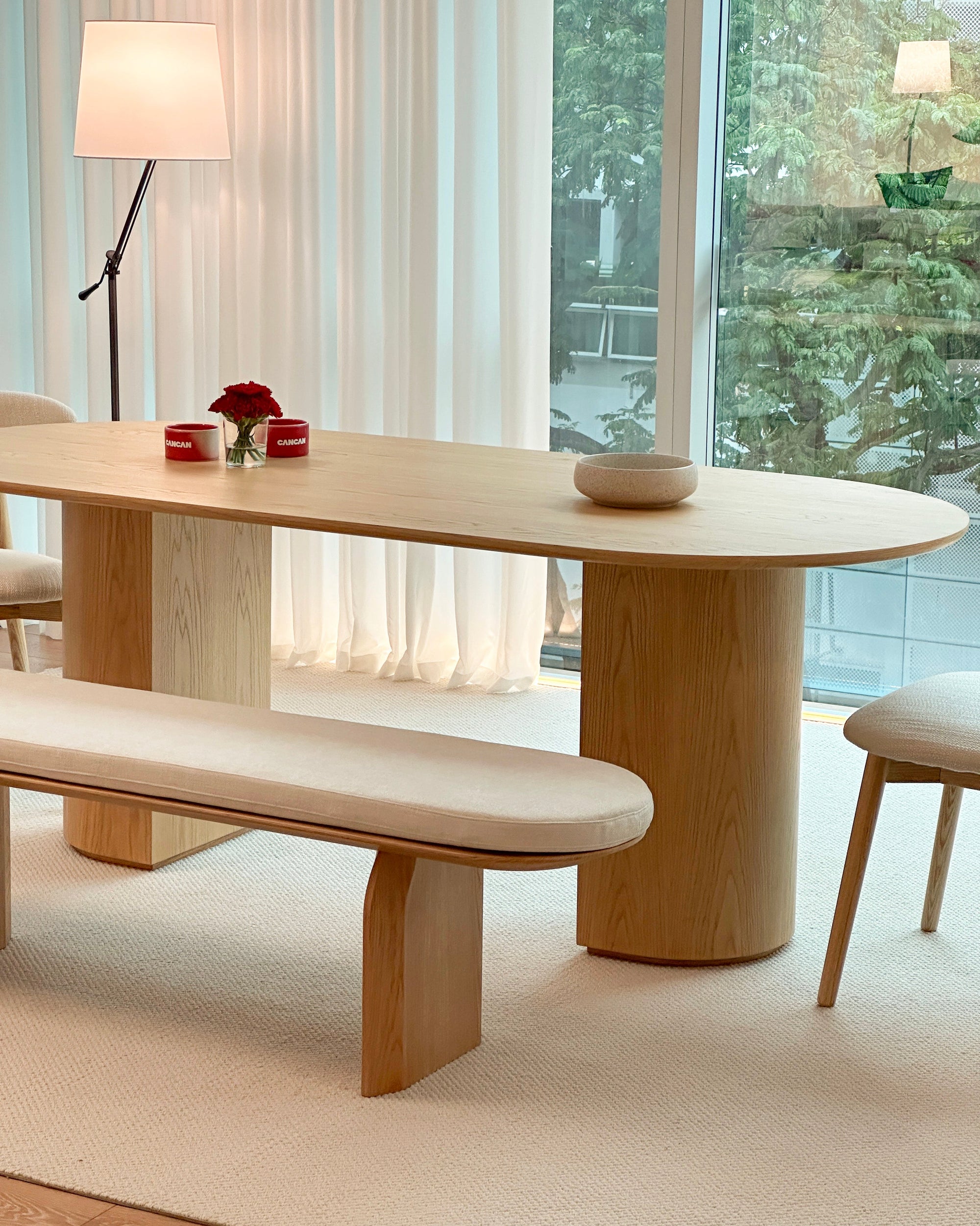 Modern dining room with wooden table and bench in a bright room with large windows.