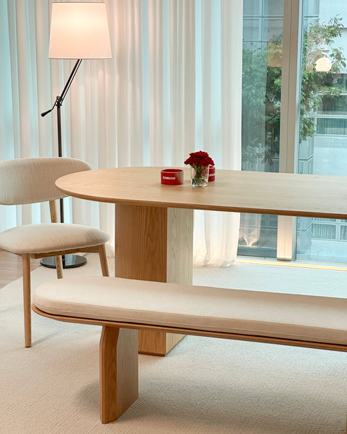 Modern dining area with wooden table, chairs, and bench in a bright room.