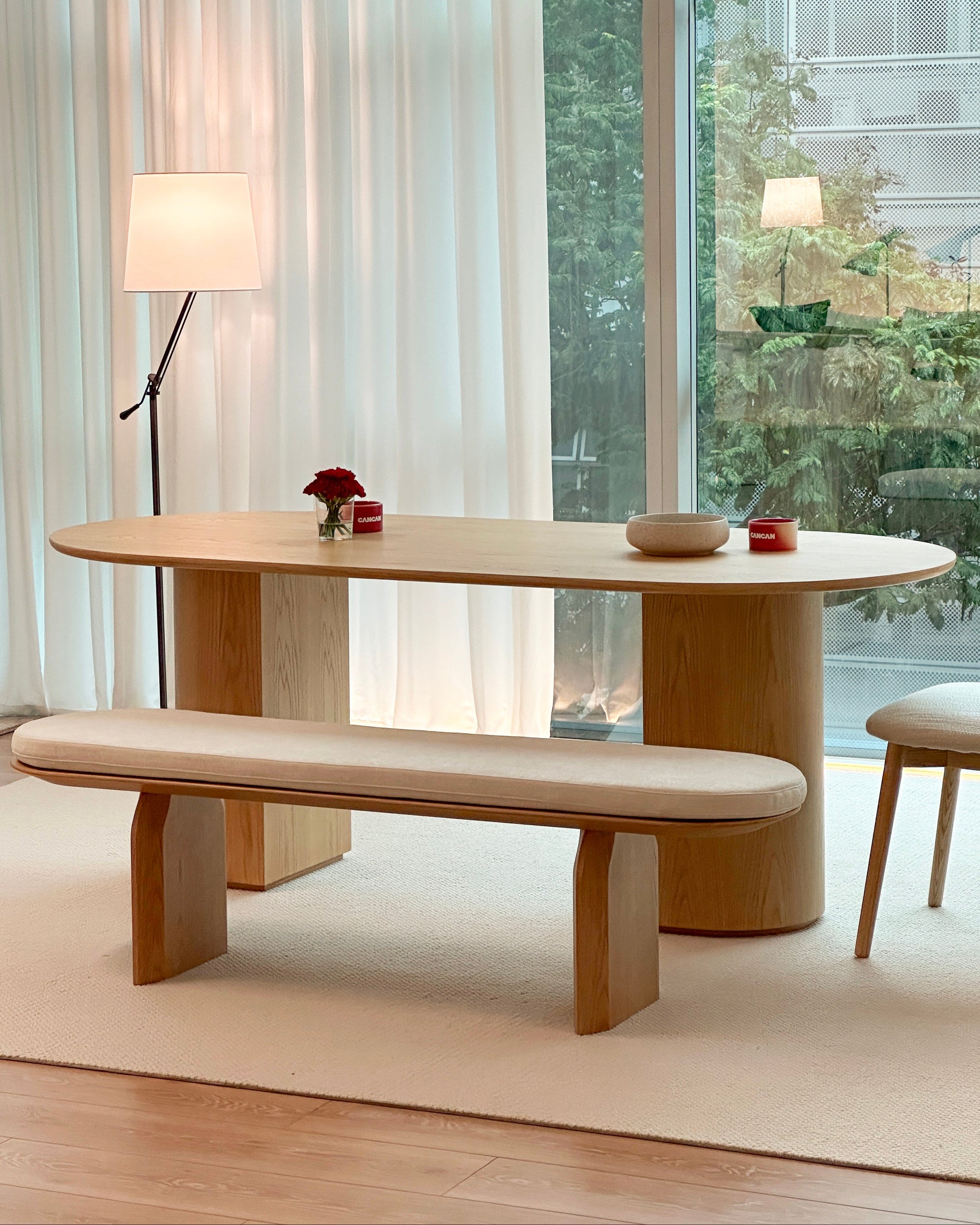 Modern dining room with a wooden table and bench in front of large windows.