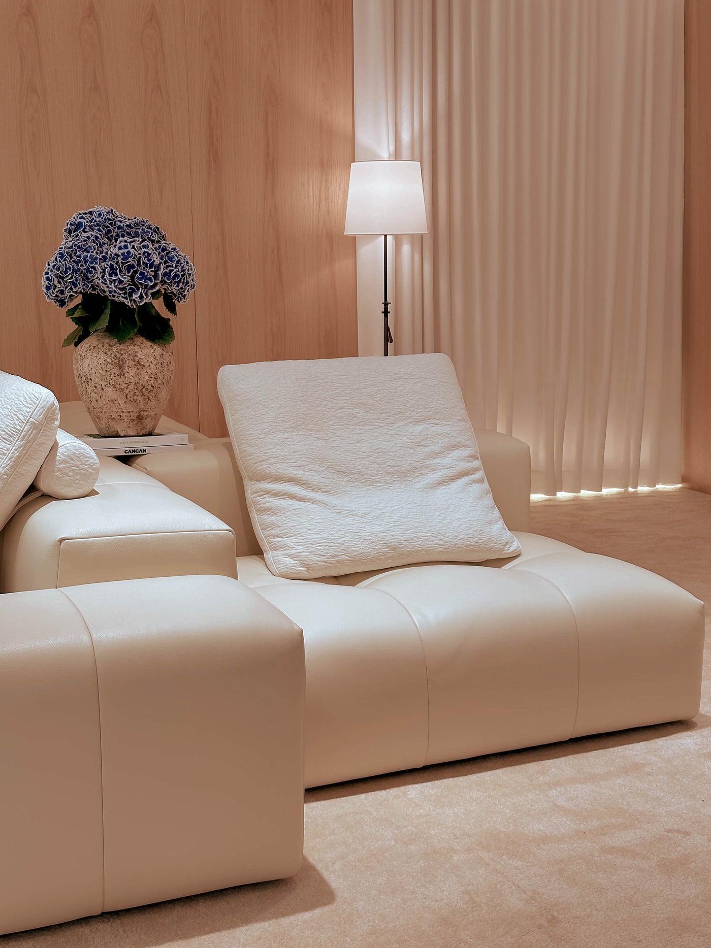 Beige sofa with a lamp and decorative plant in a room with wooden walls and curtains.
