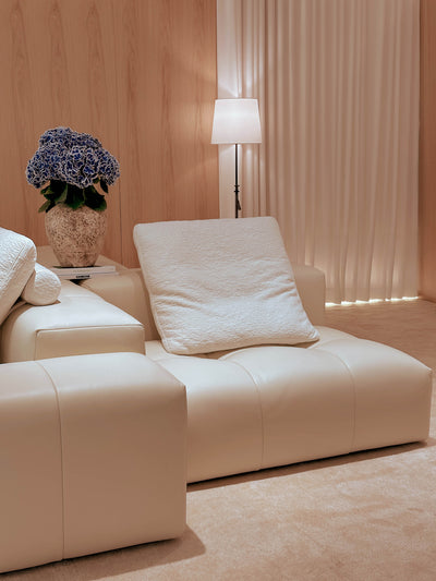 Beige sofa with a lamp and decorative plant in a room with wooden walls and curtains.