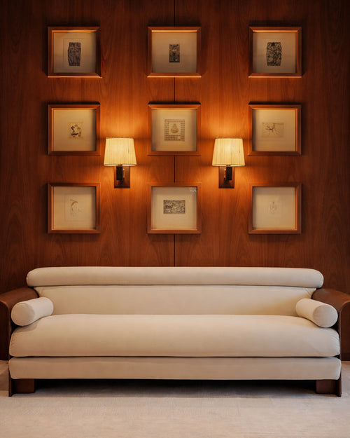 White sofa in front of a wall with framed pictures and two lamps.