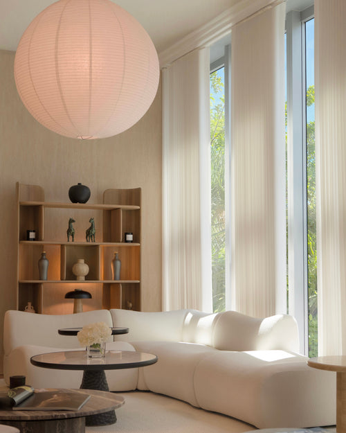 Modern living room with a white sofa, wooden bookshelf, and large windows.