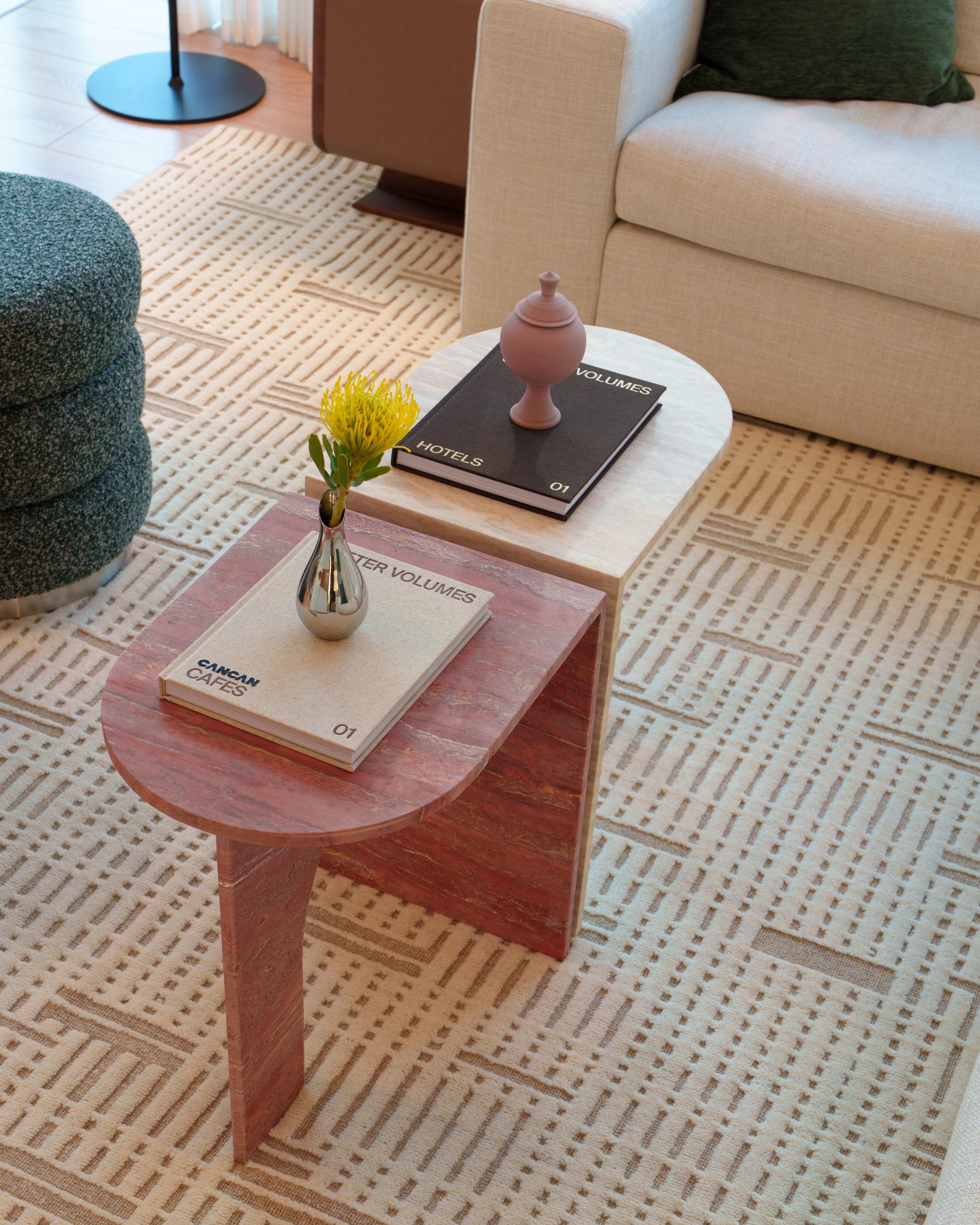 Small travertine table with books and a vase on a patterned carpet in a living room.
