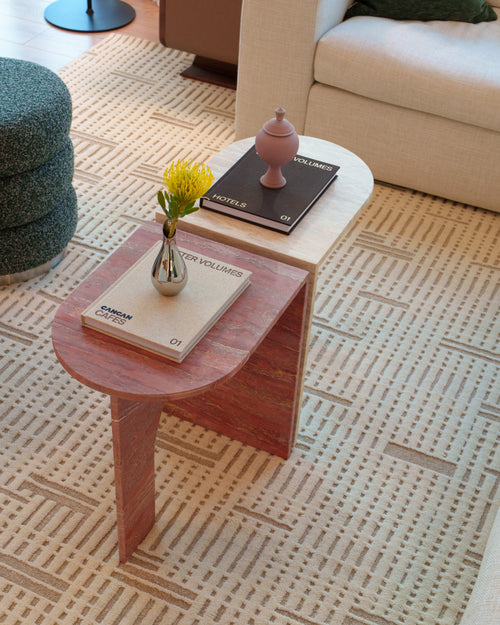 Small travertinen table with books and a vase on a patterned carpet in a living room.
