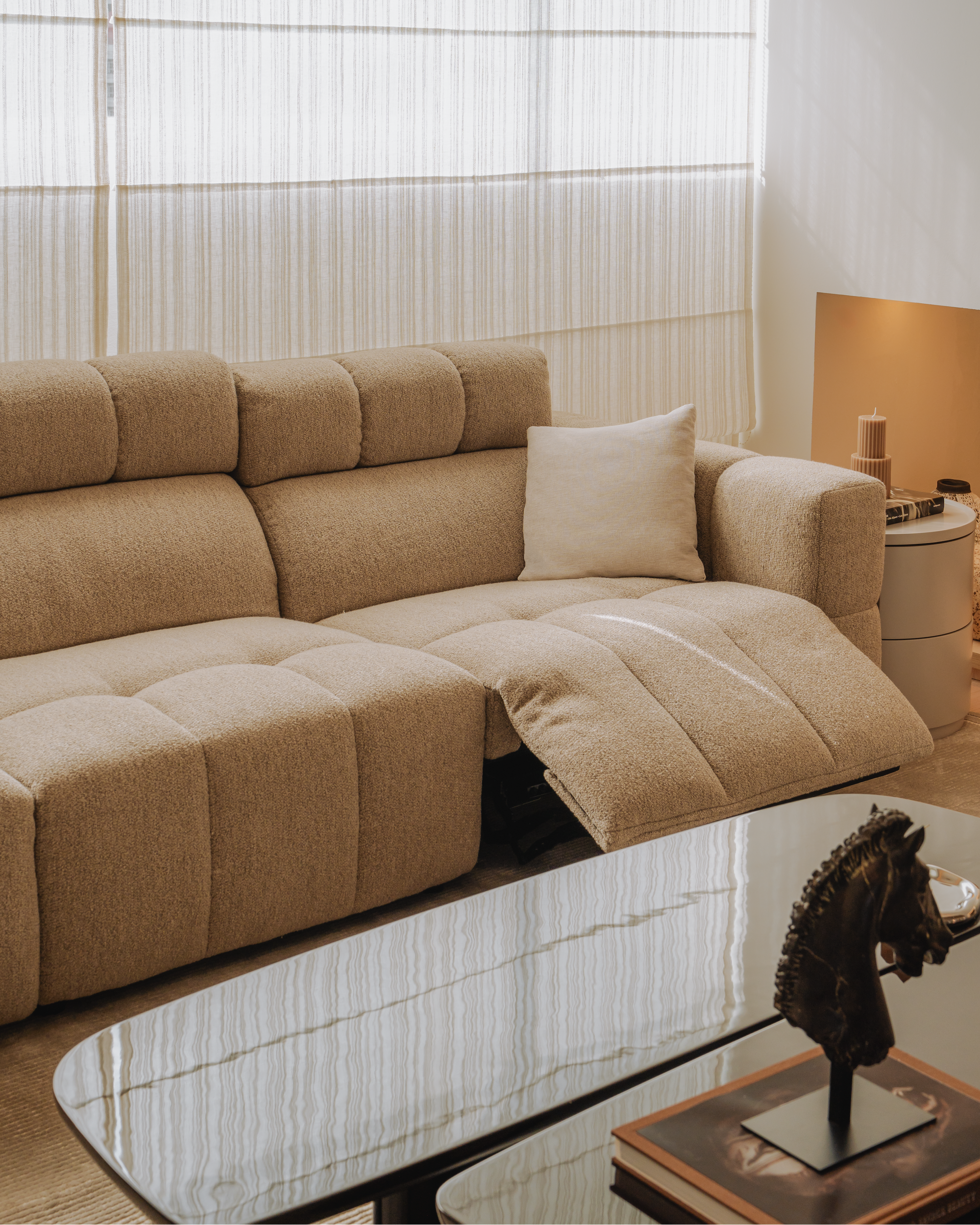 Beige sectional sofa in a living room with a glass coffee table and decorative items.