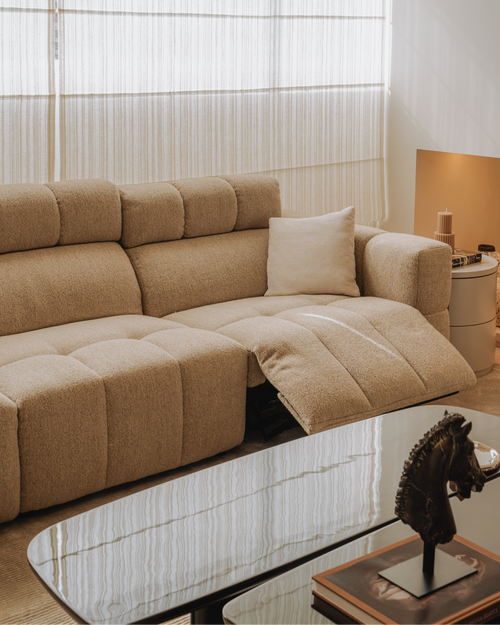 Beige sectional sofa in a living room with a glass coffee table and decorative items.