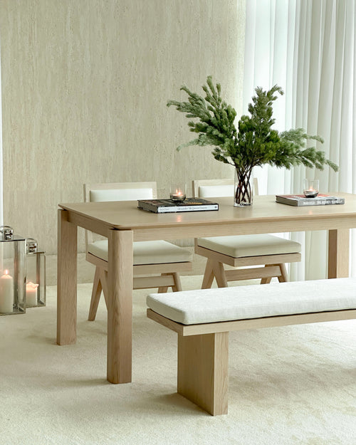 Dining room with wooden table, chairs, and bench against a neutral wall.