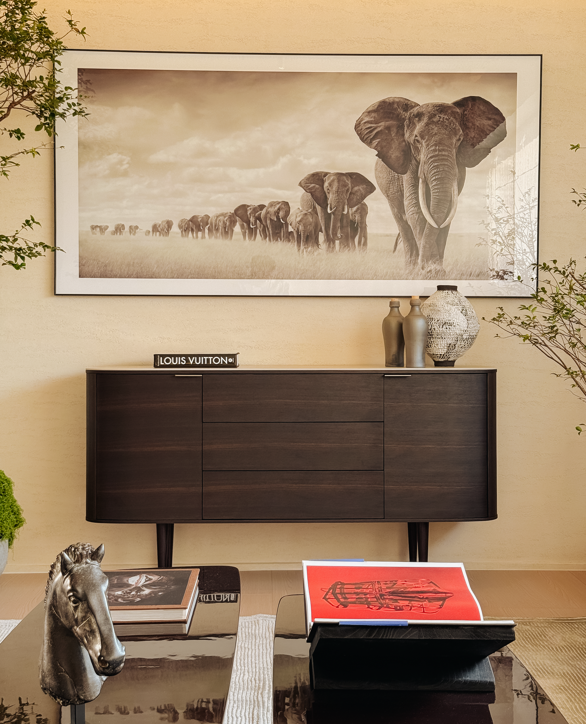 Decorative setting with a framed artwork of elephants, a Louis Vuitton box, and a horse figurine on a table.