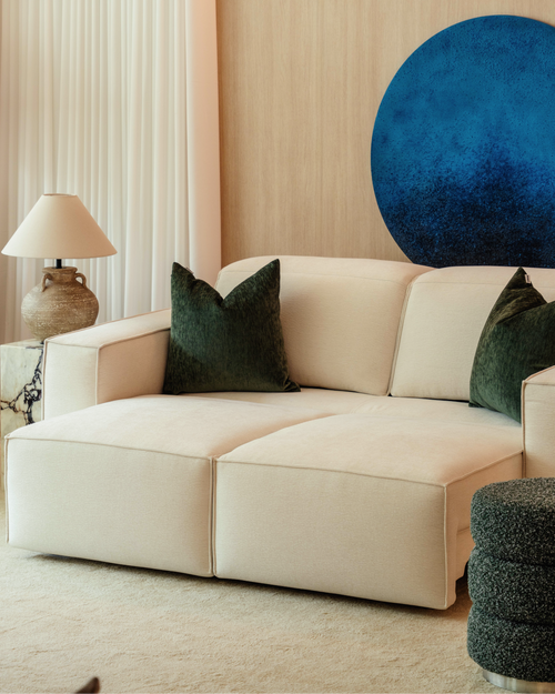 Beige sofa with green cushions in a room with a blue wall and lamp.