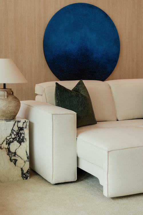 Beige sofa with a green pillow against a wooden wall with a blue circular artwork.