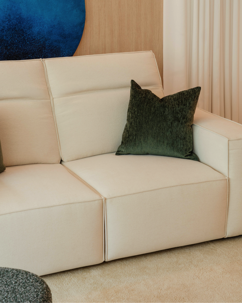 Beige sofa with a green pillow against a neutral wall with a blue circular art piece.