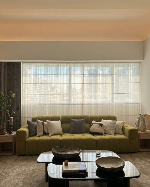 Modern living room with a green sofa, glass coffee table, and large windows.