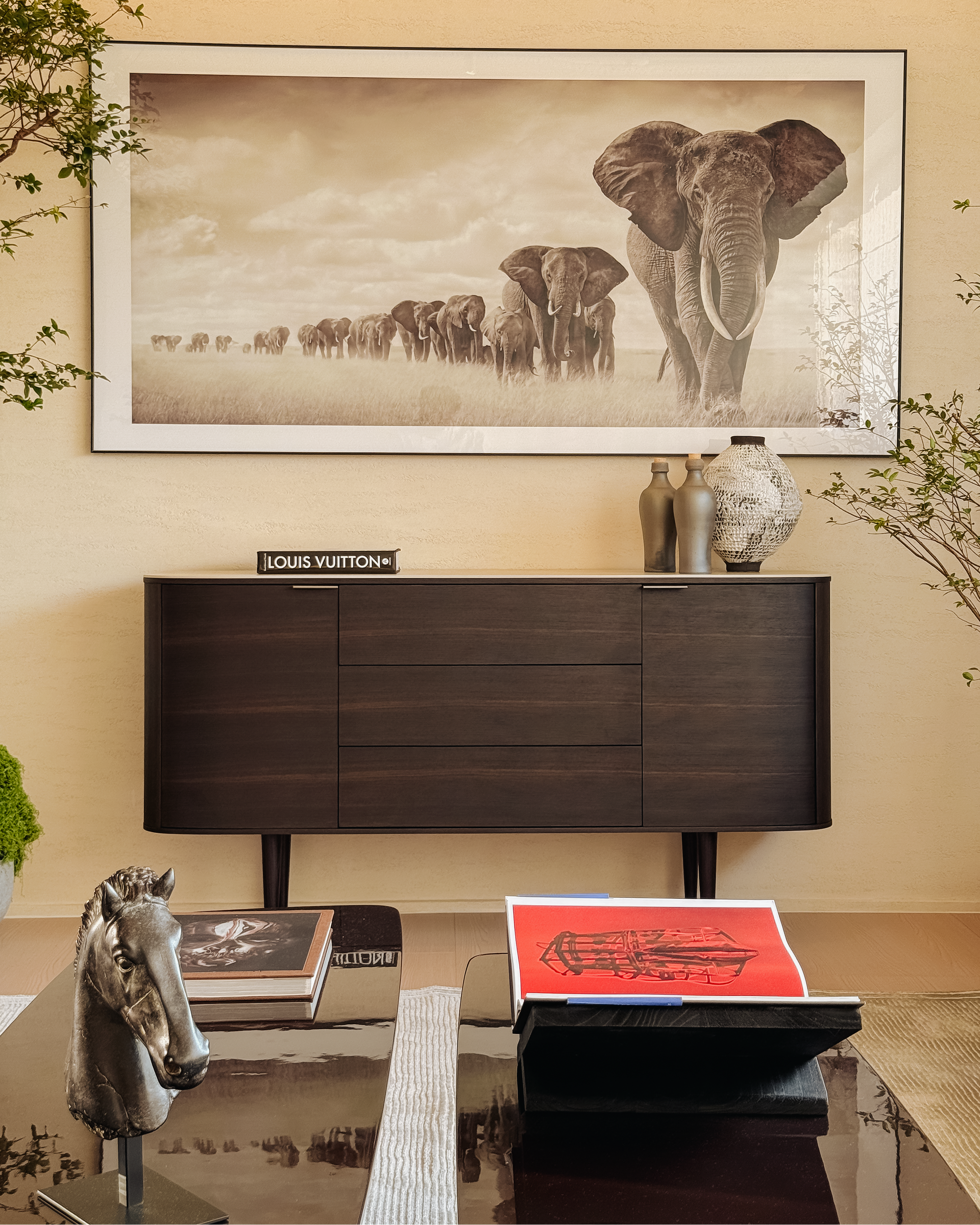 Decorative interior with a large framed picture of elephants, a Louis Vuitton box, and a horse sculpture.