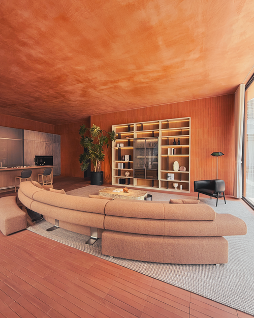 Modern living room with a curved beige sofa, wooden floor, and bookshelf.
