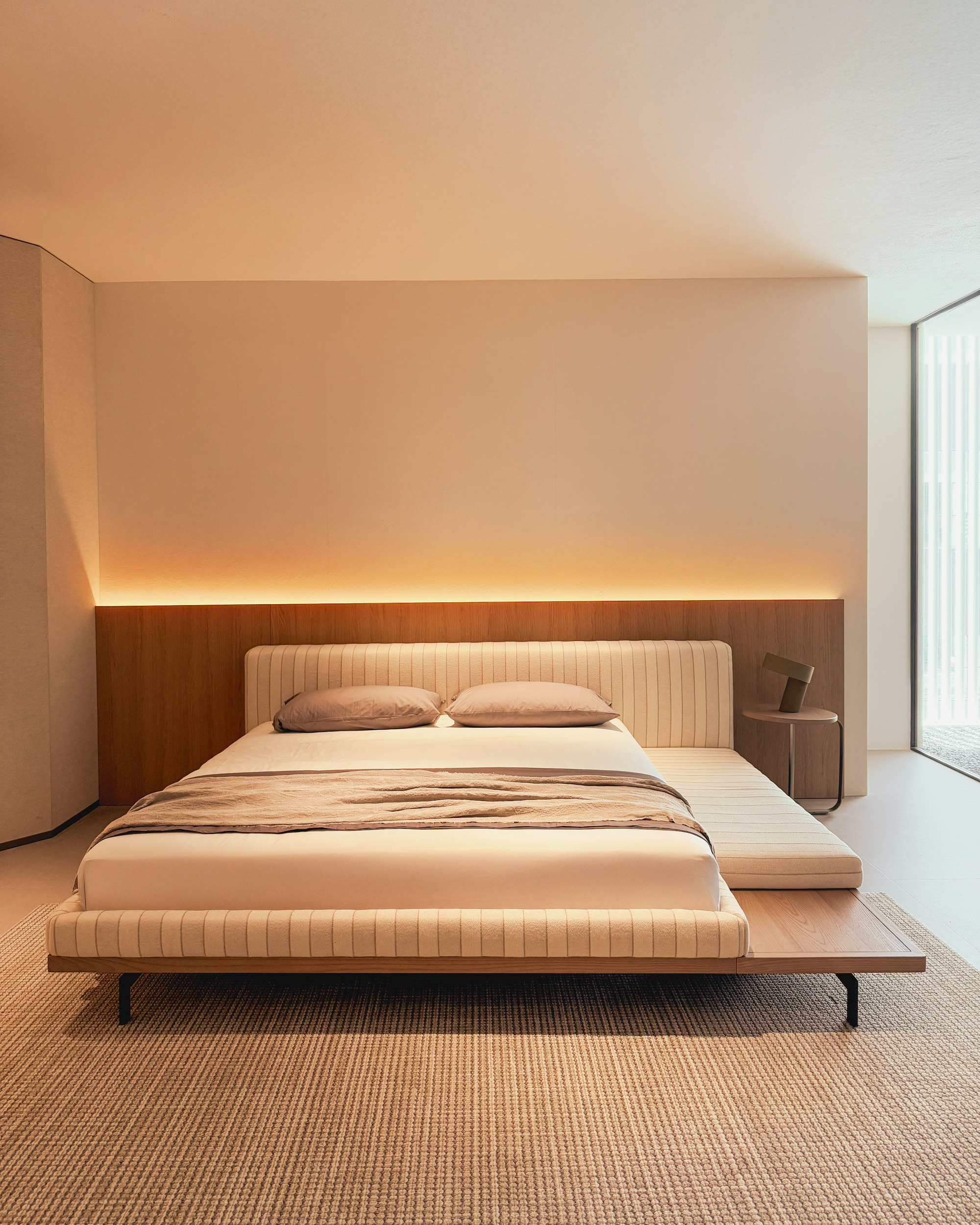 Modern bedroom with a bed and wooden headboard against a neutral wall.