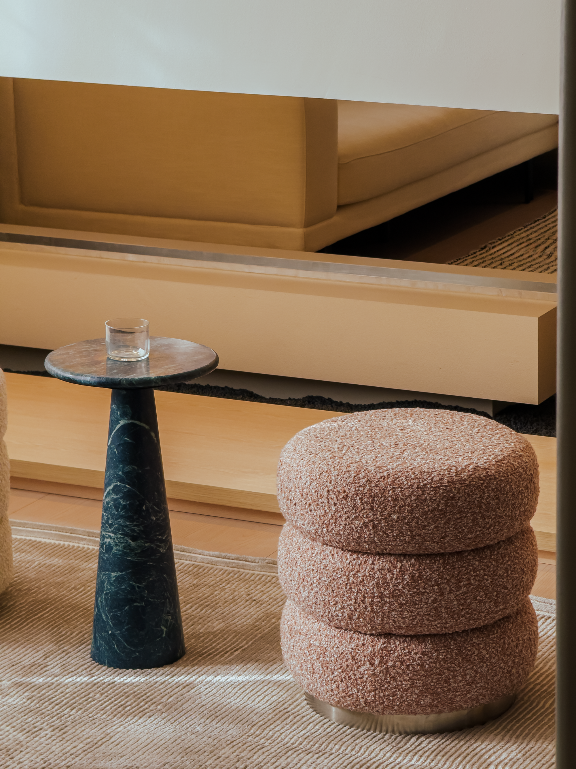 Decorative table with a glass and textured ottoman in front of a fireplace.