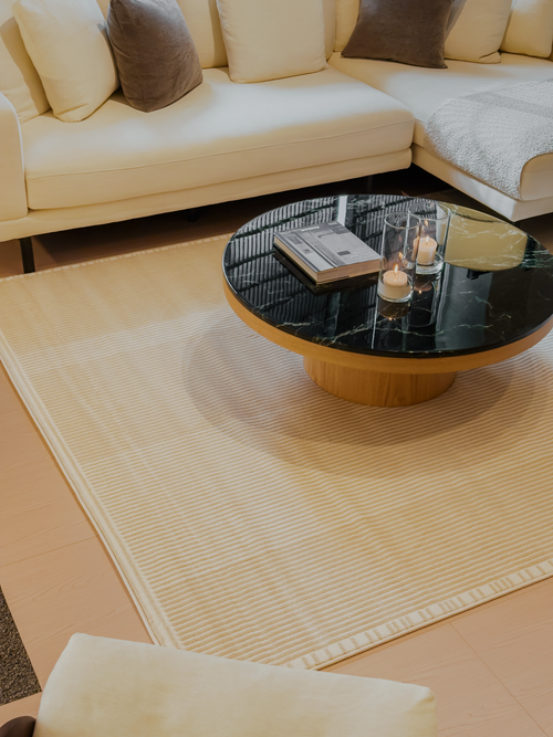 Round coffee table with decorative items on a beige rug in a living room setting.
