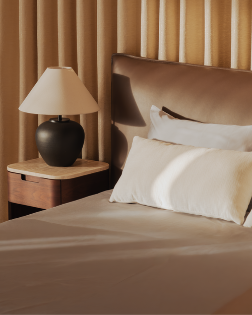 Bedroom with a bed, nightstand, and lamp against a beige curtain.