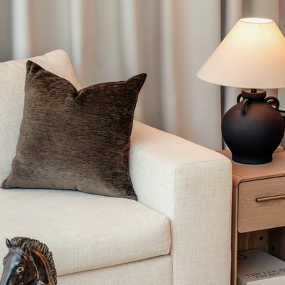 Beige sofa with a brown pillow, wooden side table with lamp, and decorative horse head sculpture in a living room setting.
