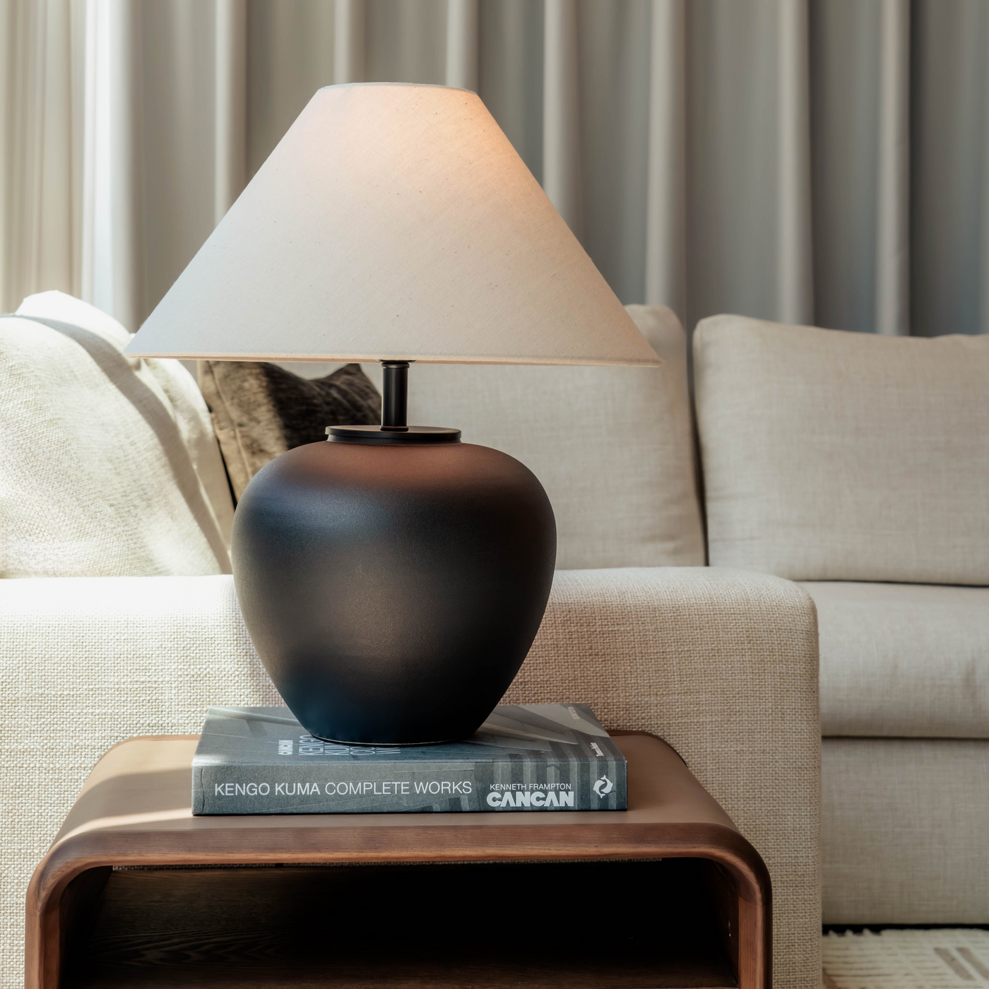 Black lamp with a white shade on a wooden side table in a living room setting.