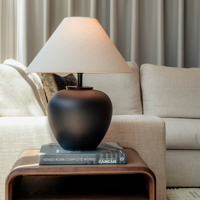 Black lamp with a white shade on a wooden side table in a living room setting.