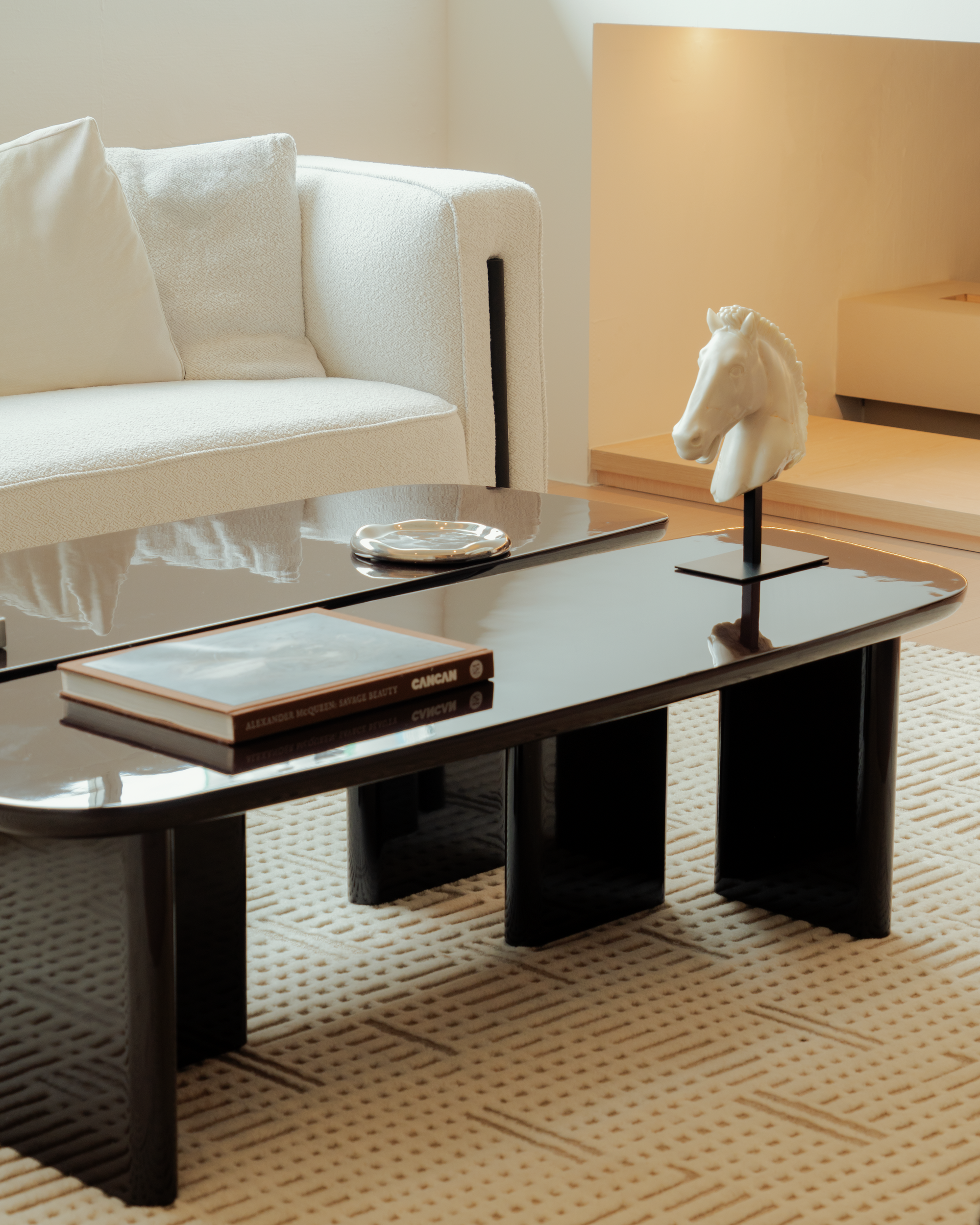 Modern living room with a black coffee table, white sofa, and decorative horse sculpture.