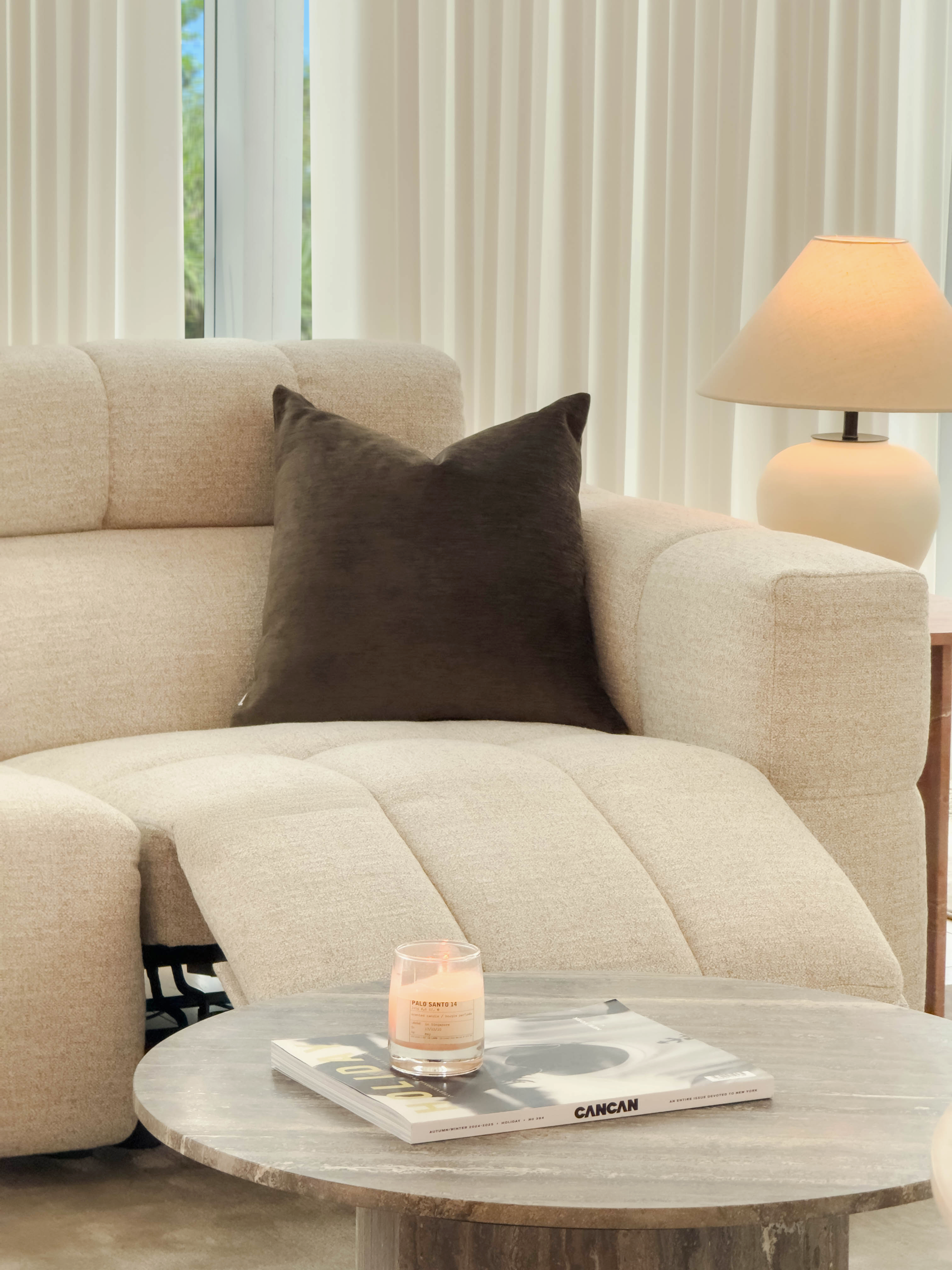 Beige sofa with a brown pillow and a small table with a candle and magazine in a living room.