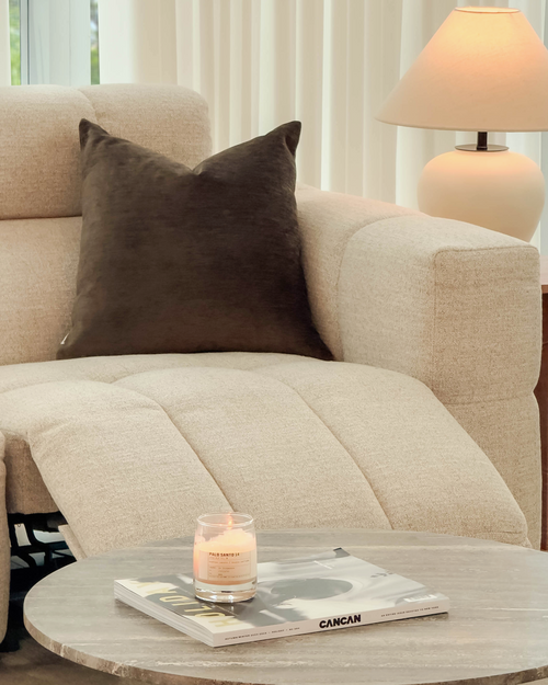 Beige sofa with a brown pillow and a wooden coffee table with a candle and magazine in a living room.
