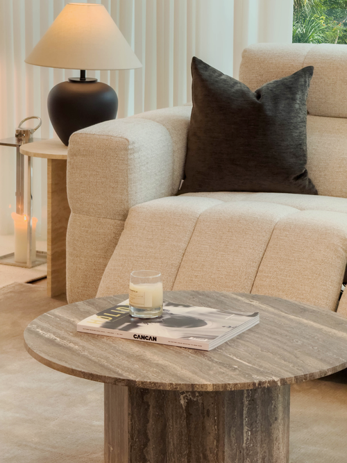Beige sofa with a brown pillow and a wooden coffee table with a glass of milk and magazine.