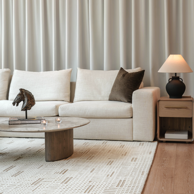 Modern living room with a beige sofa, wooden coffee table, and side table against a neutral wall.