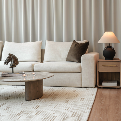 Modern living room with a beige sofa, wooden coffee table, and side table against a neutral wall.