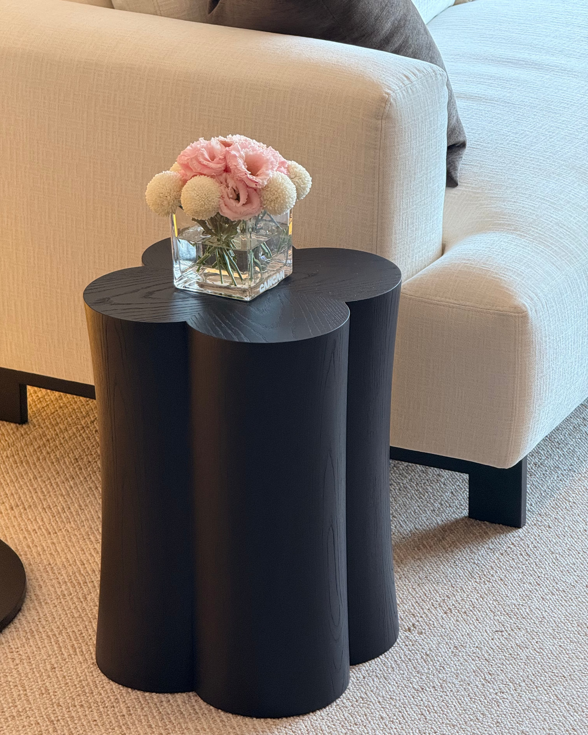 Black side table with a glass vase of flowers on a beige sofa
