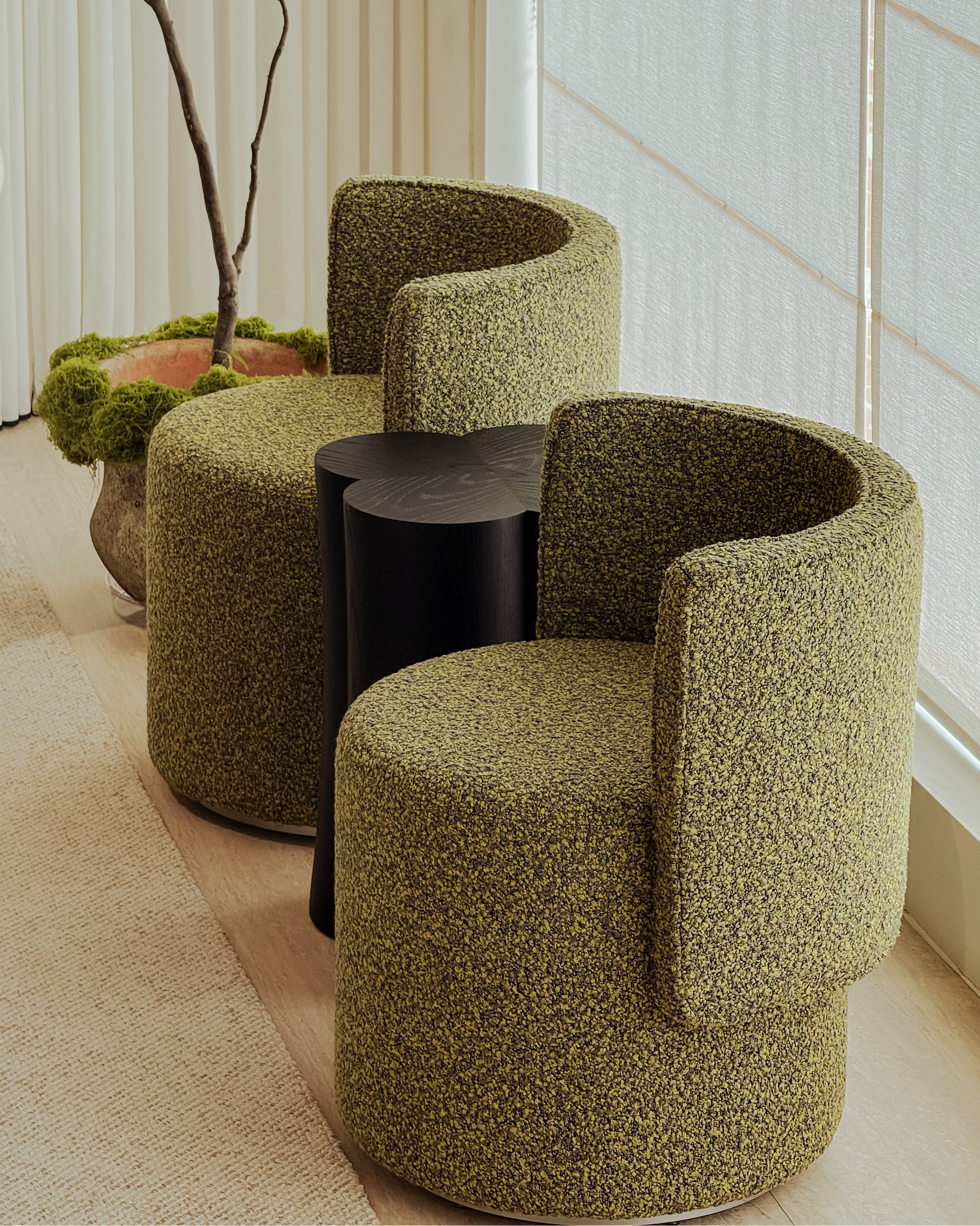 Three green textured chairs around a black round table in a room with large windows.