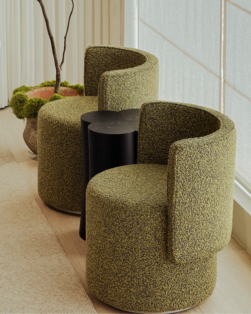 Three green textured chairs around a black round table in a room with large windows.