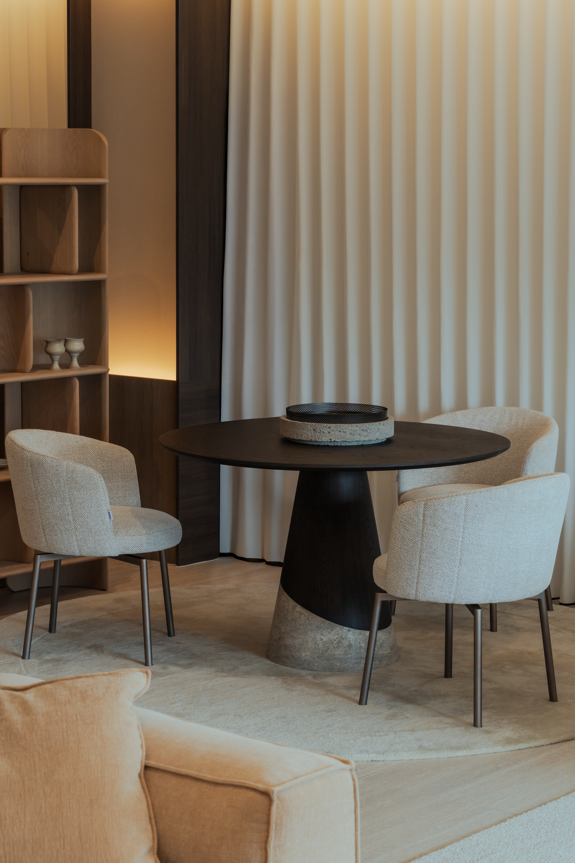 Modern dining area with a round black table and beige chairs in a softly lit room.