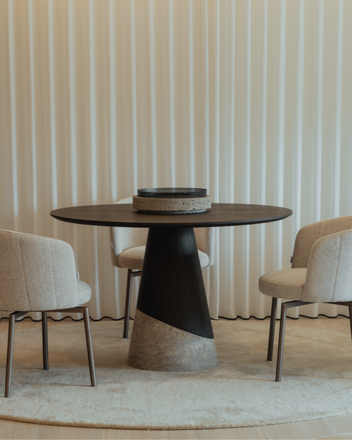 Modern dining table with a black and gray base and beige top, surrounded by chairs against a striped wall.