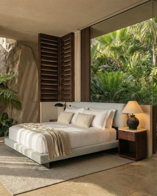 Modern bedroom with a large bed, nightstands, and a view of greenery outside.