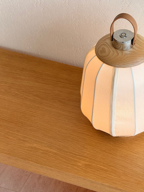 Decorative lamp with wooden handle on a wooden surface against a textured wall.