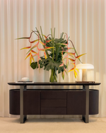 Modern dark brown sideboard with a vase of flowers and a lamp against a beige curtain background