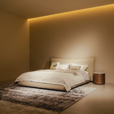 Modern bedroom with a bed and side table against a beige wall with ambient lighting.