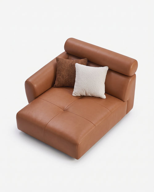 A modern low-profile leather daybed or chaise lounge in warm tan-brown, styled with two throw pillows (one textured brown, one cream) on a seamless white background.